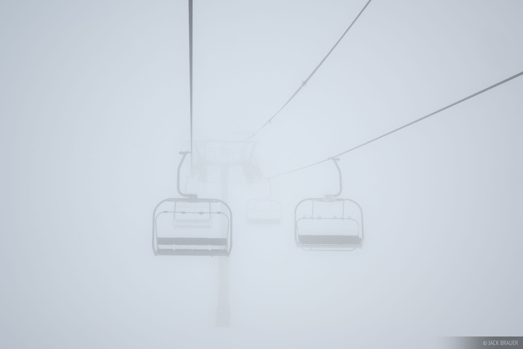 Empty chairlift in a foggy snowstorm.