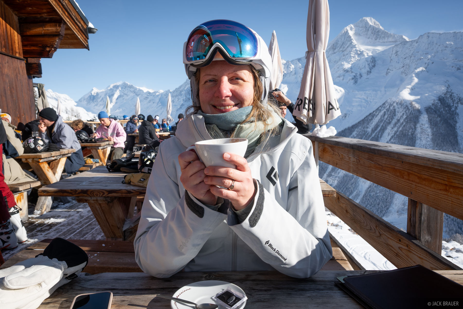A skier drinks a cappucinno on the deck of a chalet in winter in the Swiss Alps